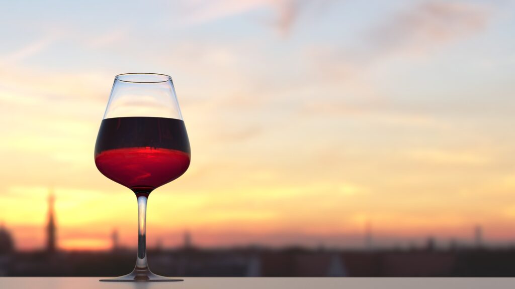 A glass of red wine with a sunset in the background, symbolizing the elegance and tradition of French wine.