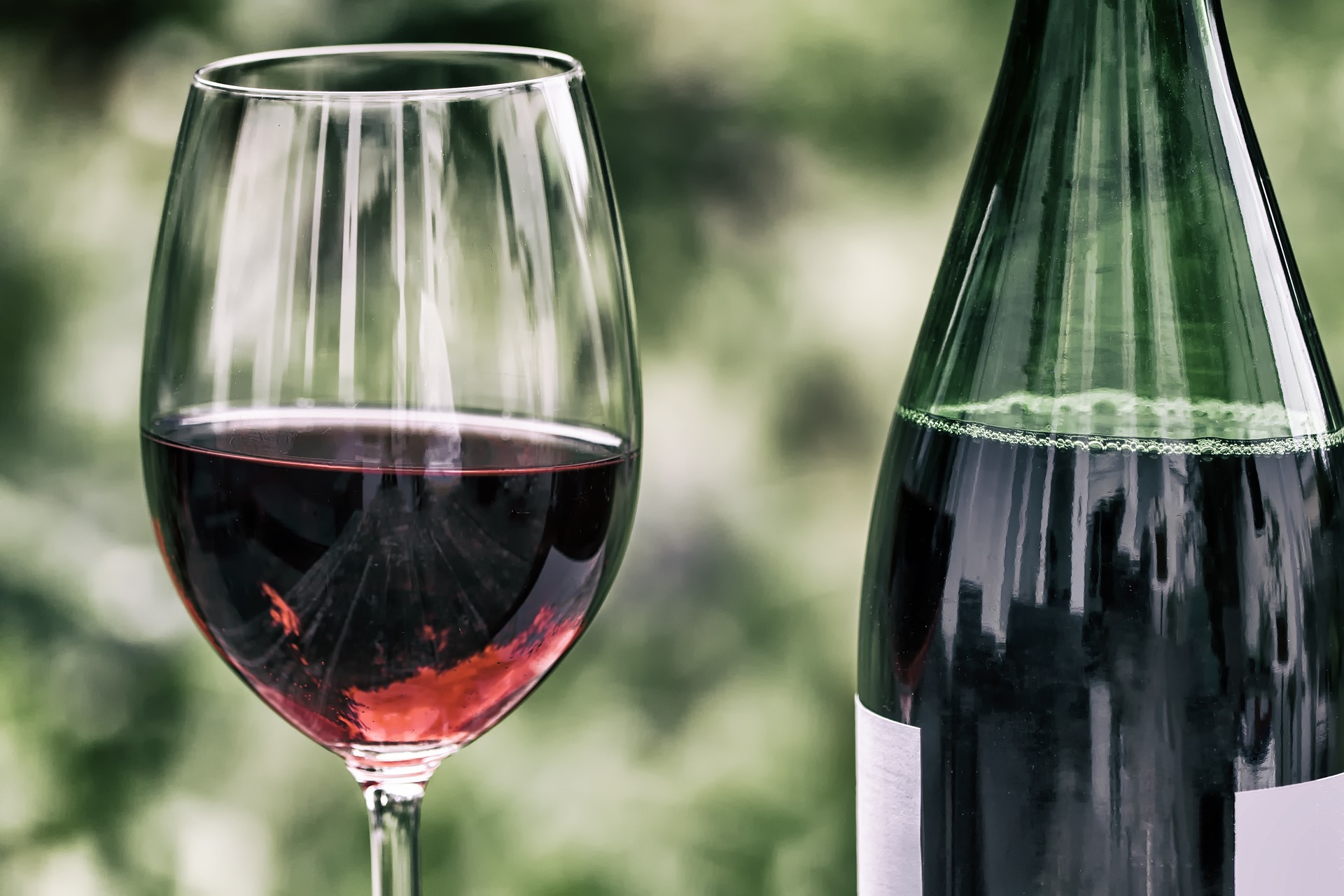 Glass of red wine and wine bottle outdoors with green background