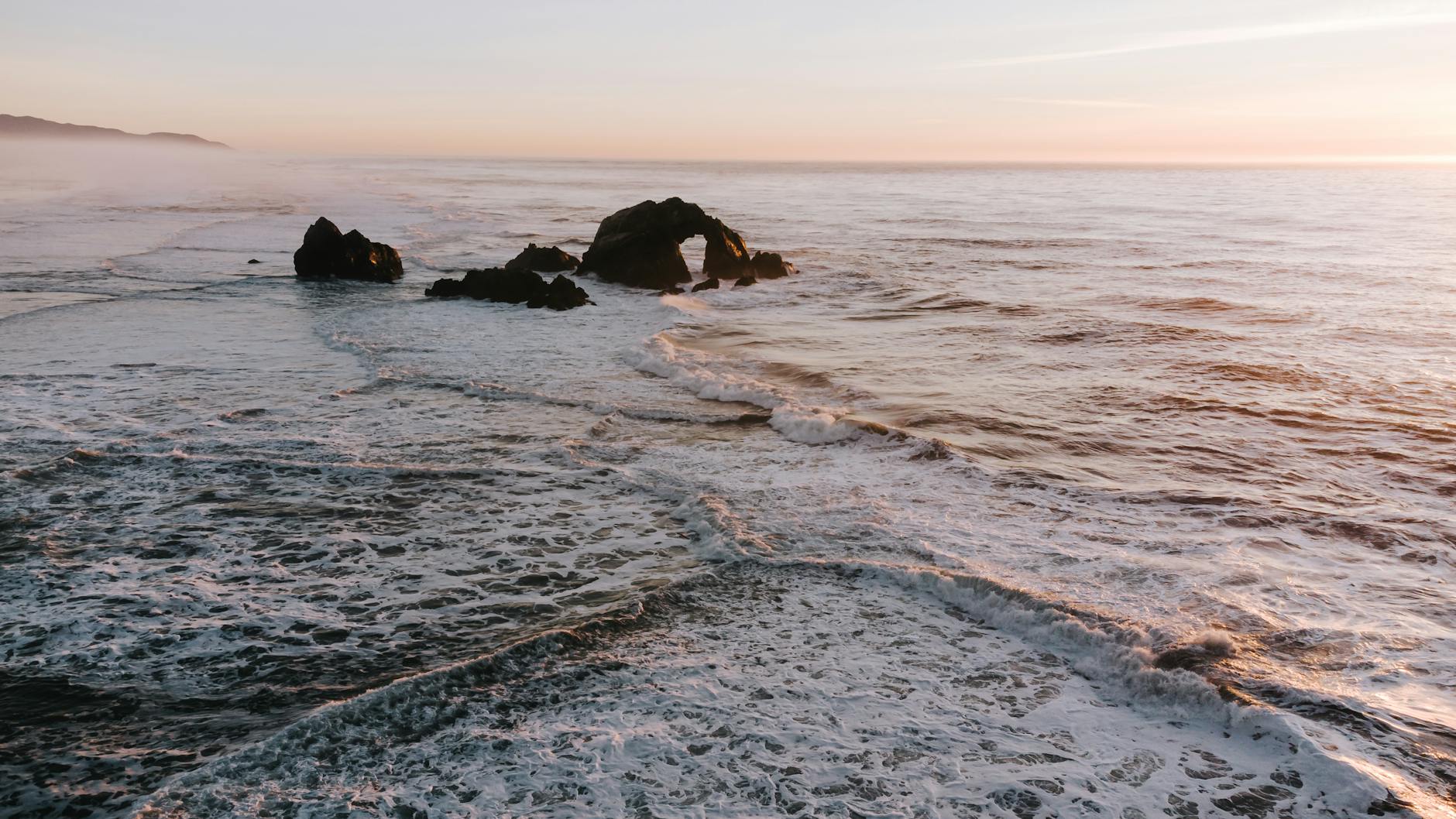 A rocky coastal scene at sunset along the California coast, symbolizing the dry conditions impacting vineyards inland.