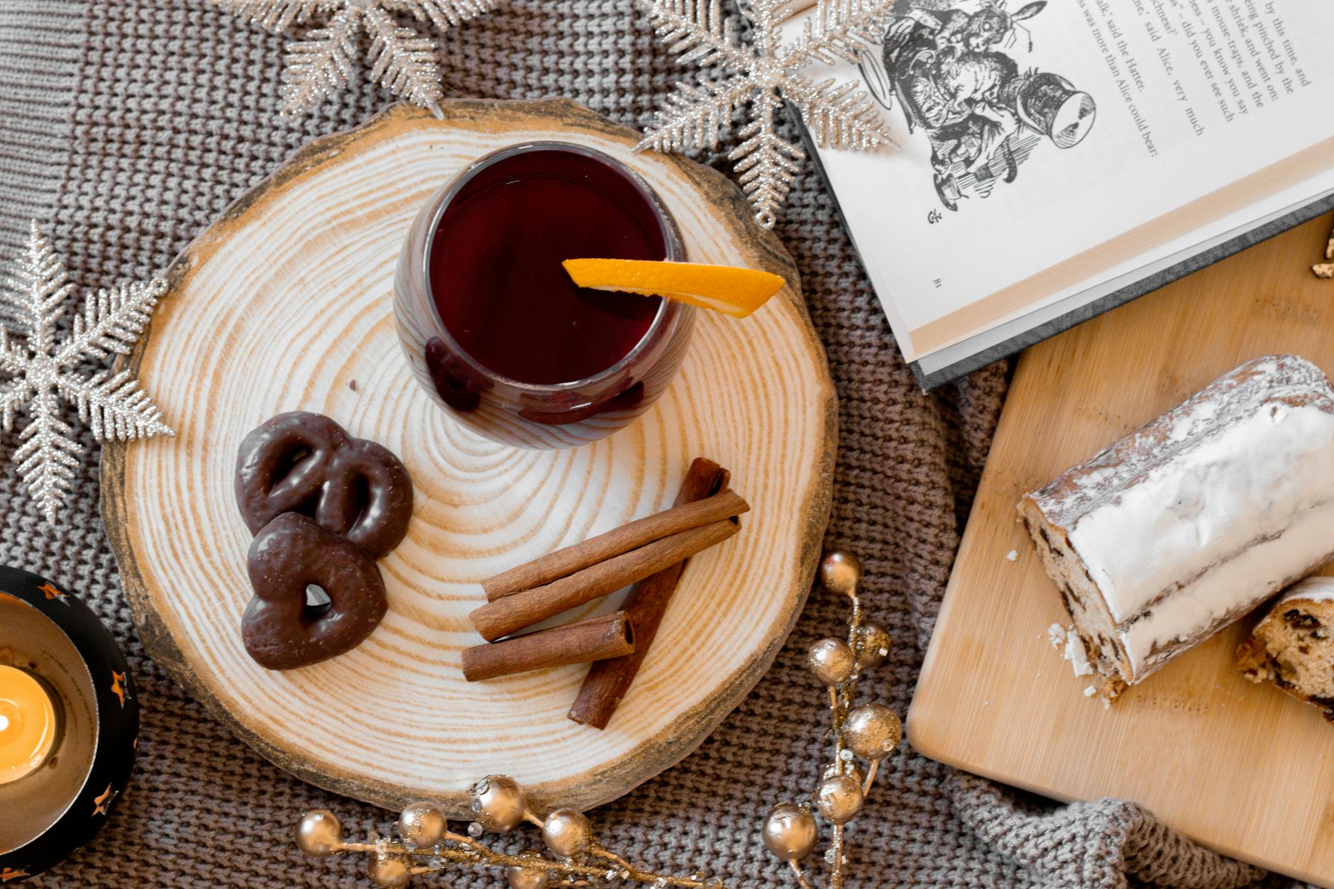 Glass of mulled red wine with cinnamon sticks and holiday treats on a wood tray