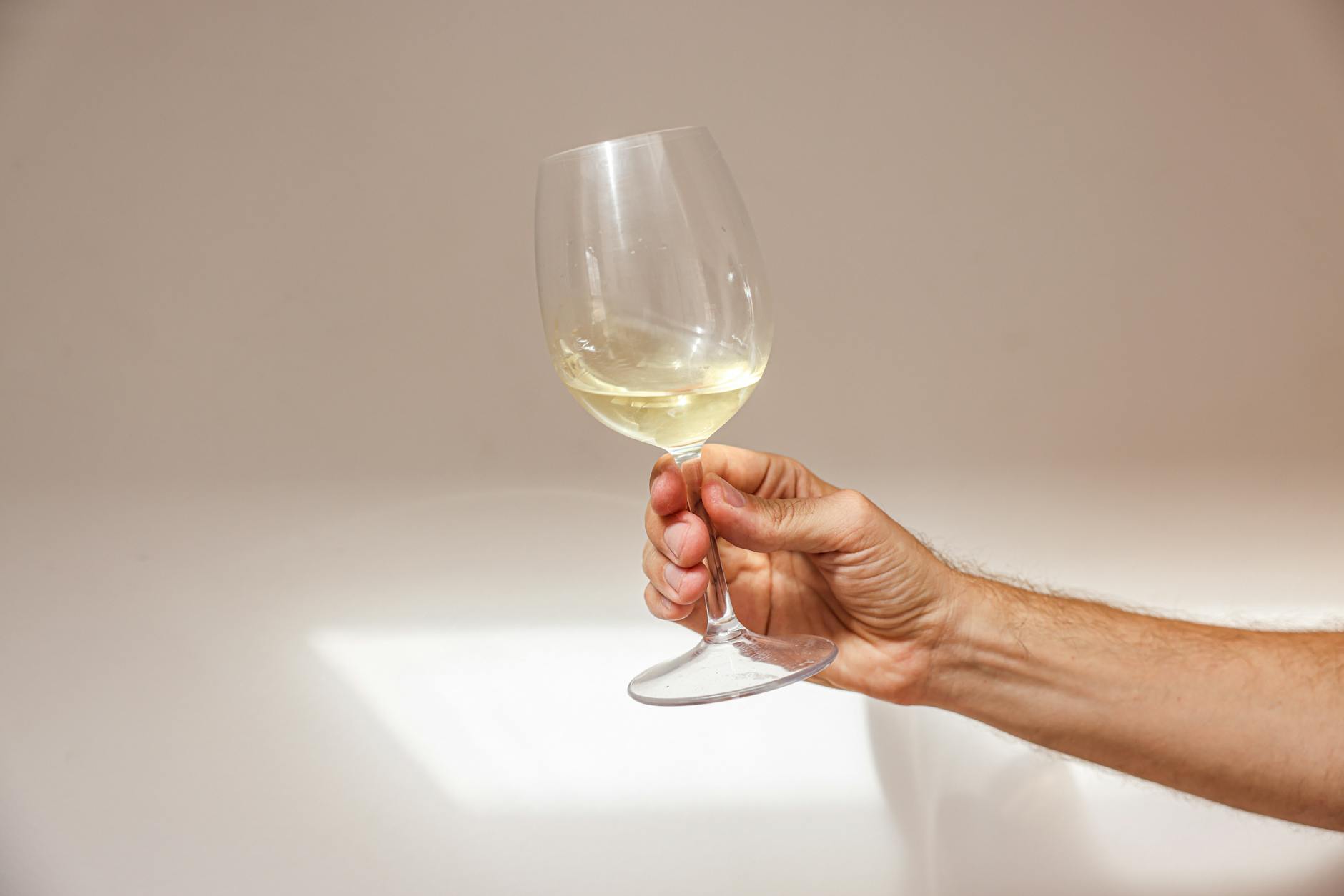 Hand holding a glass of white wine in front of a soft beige background