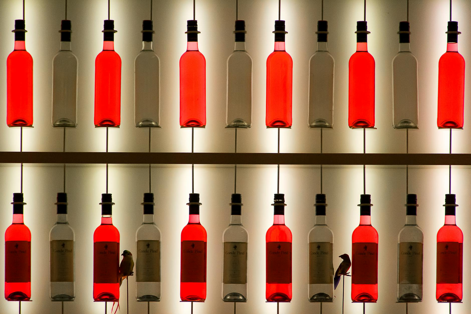 Rows of red and clear wine bottles displayed with dramatic lighting.
