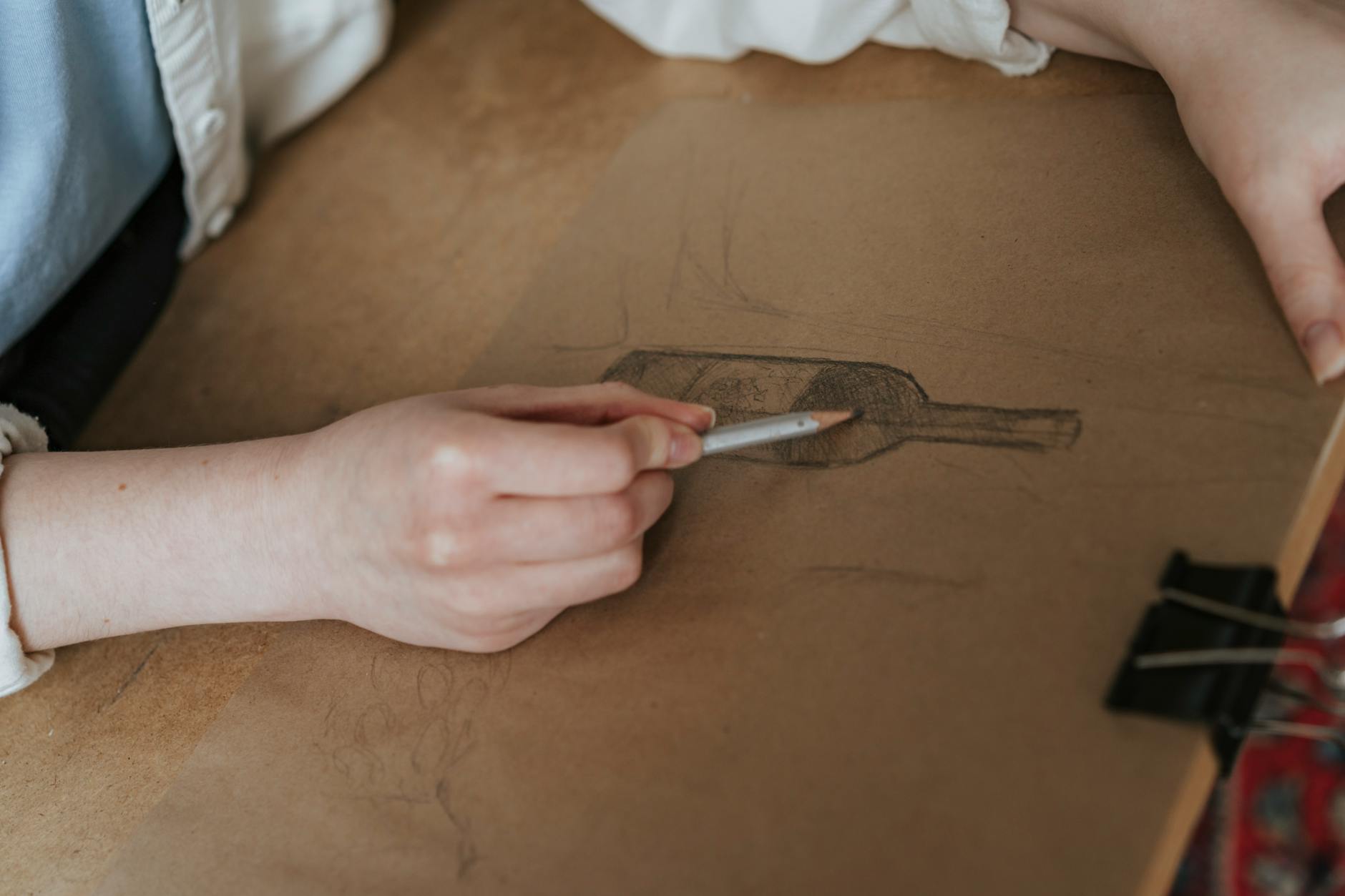 Artist sketching a wine bottle label design with pencil on brown paper.